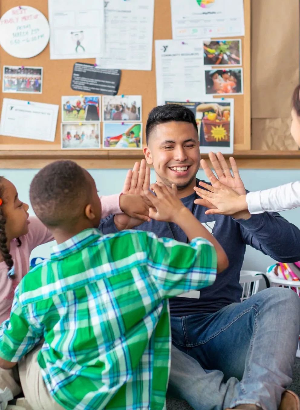 Smiling instructor high-fives three happy children during an after-school program.