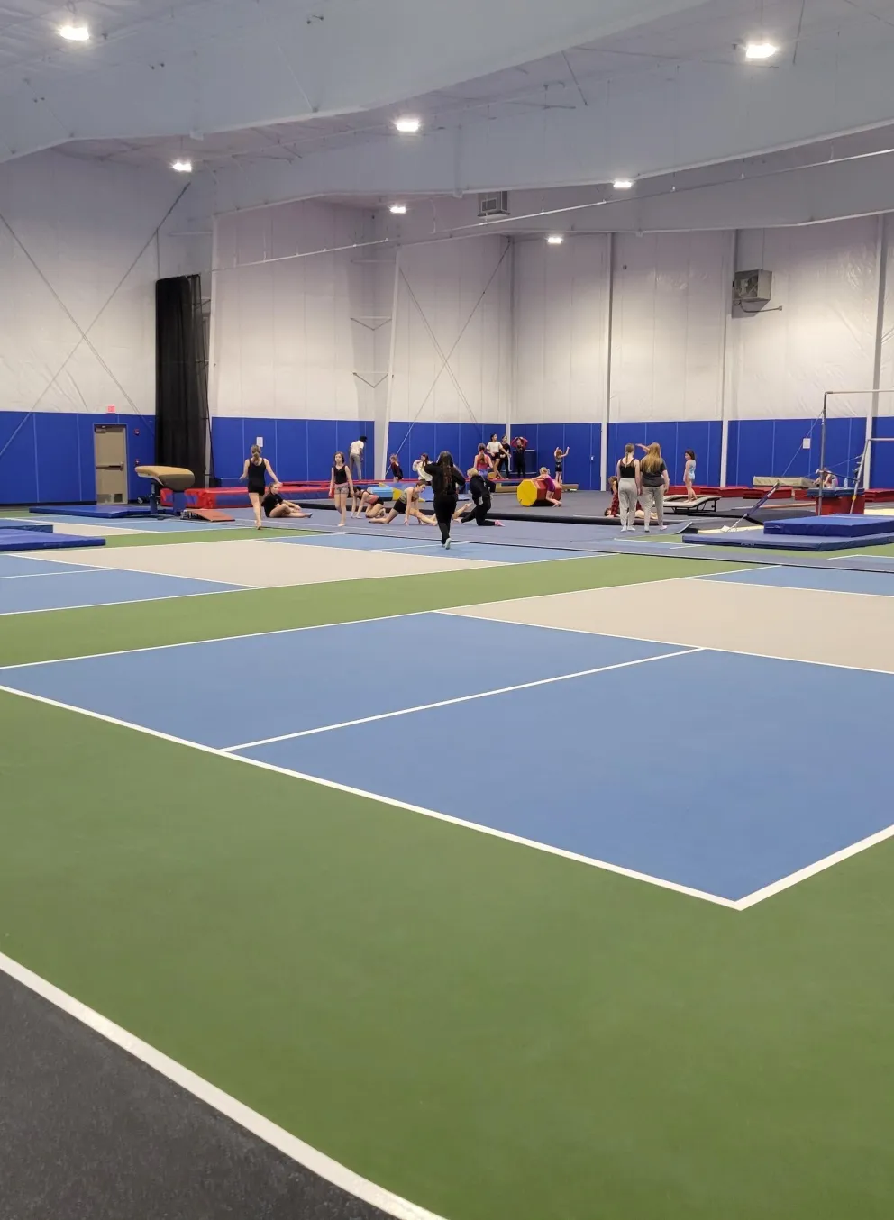 Large gym with kids' gymnastics equipment and a running track.  Several children and adults participate in activities.