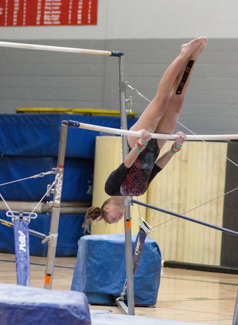 A young gymnast performs a backward handstand on uneven parallel bars during a kids' program.