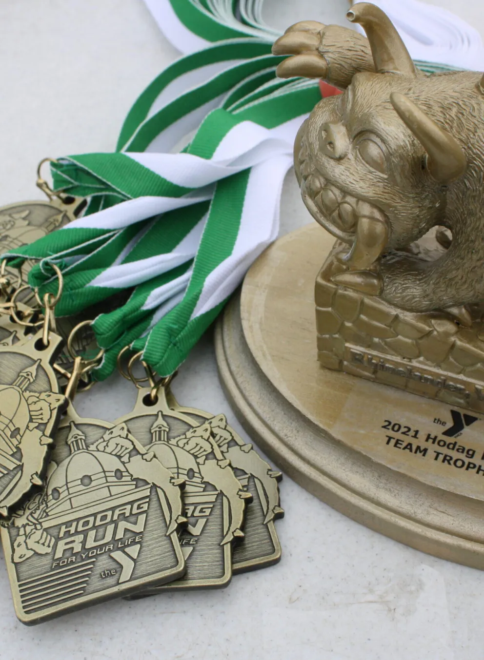Several bronze medals from a Hodag Run,  alongside a gold team trophy featuring a sculpted Hodag.  Green and white ribbons are included.