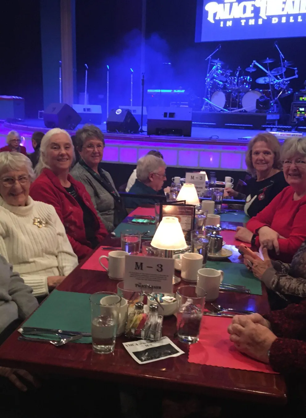 A group of women enjoy a meal together at a table in a theater.  A stage with musical instruments is visible in the background.