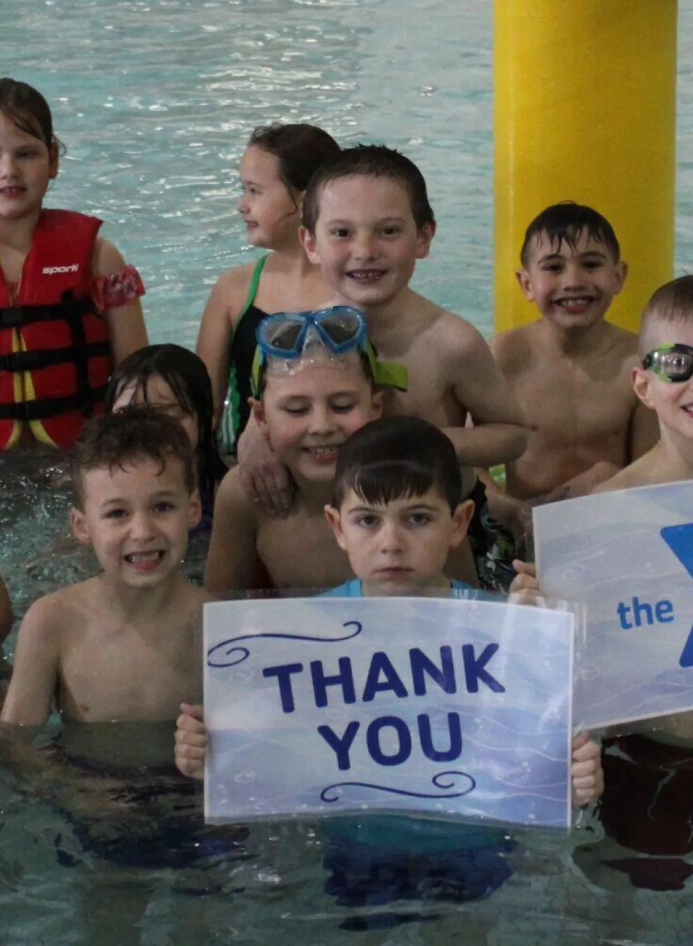 Happy children in a pool, holding signs that say "Thank You," "Northwoods United Way!", and a United Way logo.  Some wear life vests.