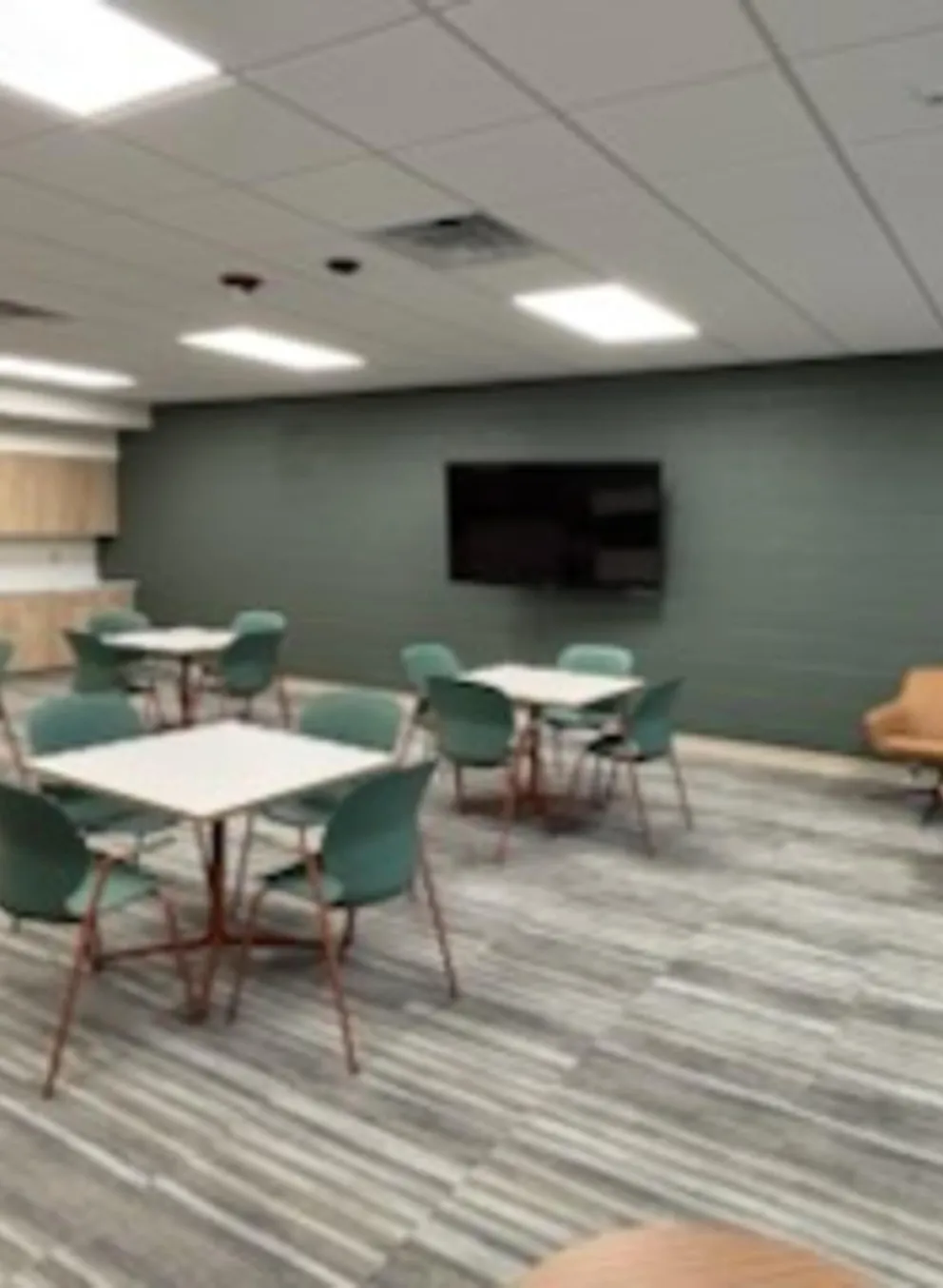 Brightly lit room with tables, chairs, a flat screen TV, and tan leather chairs for after school youth programs.