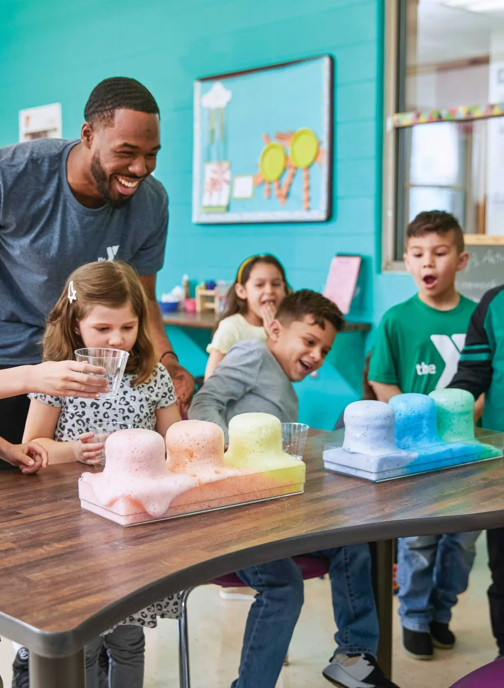 Smiling children conduct a science experiment with pastel-colored substances, guided by a cheerful instructor.
