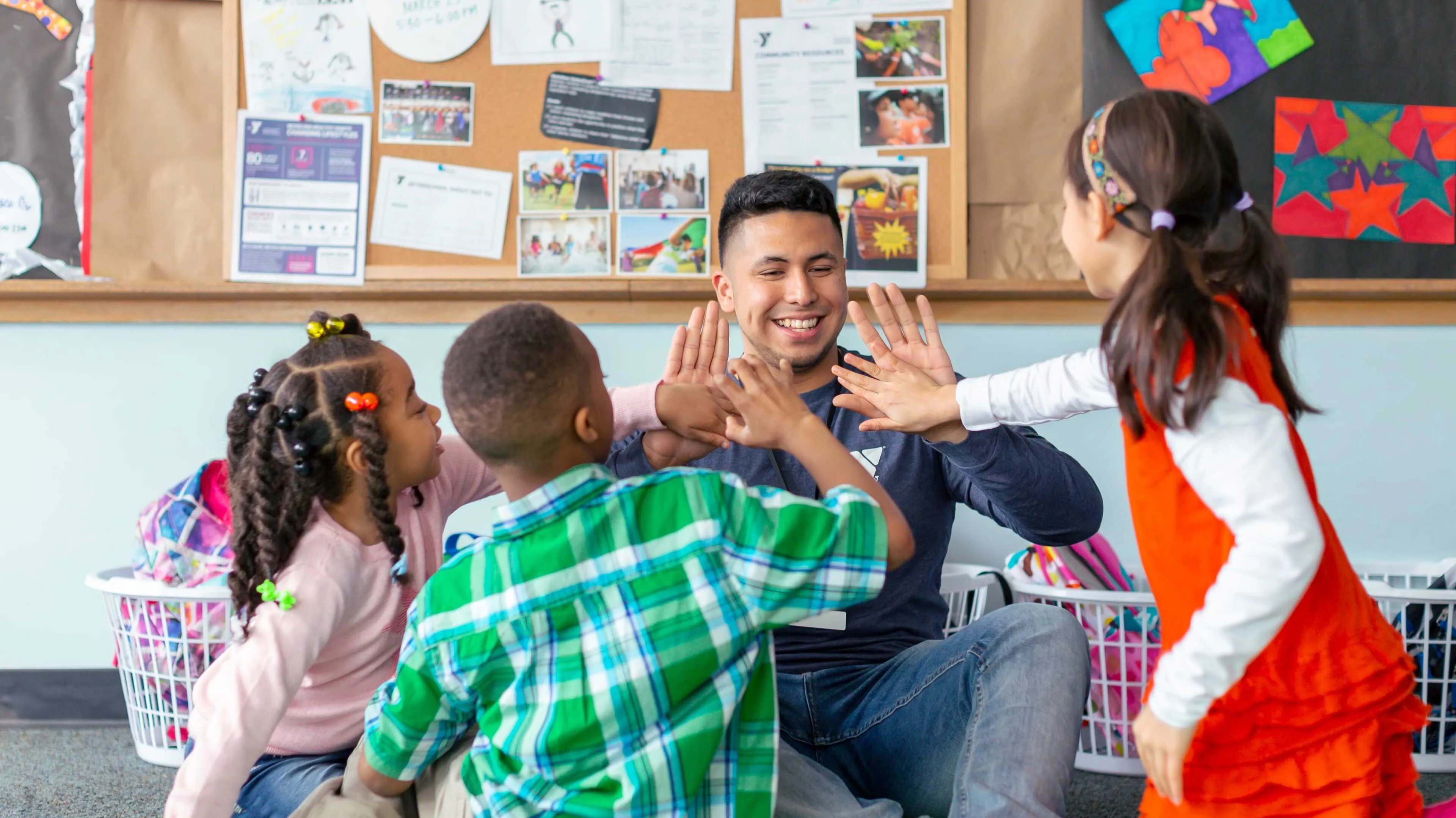 Smiling instructor high-fives three happy children during an after-school program.