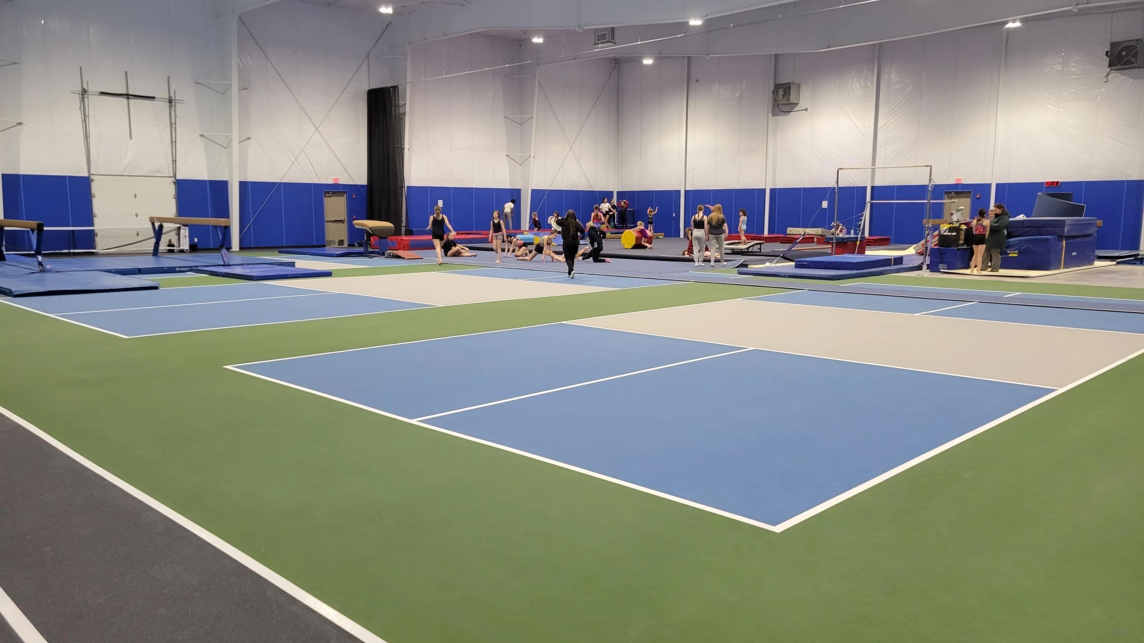 Large gym with kids' gymnastics equipment and a running track.  Several children and adults participate in activities.