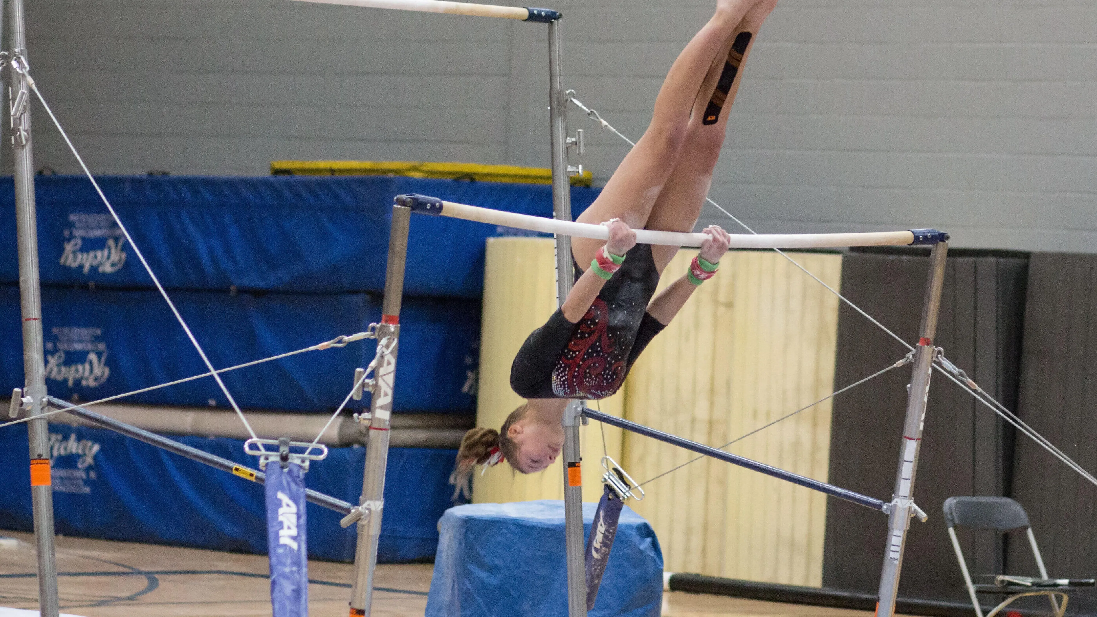 A young gymnast performs a backward handstand on uneven parallel bars during a kids' program.