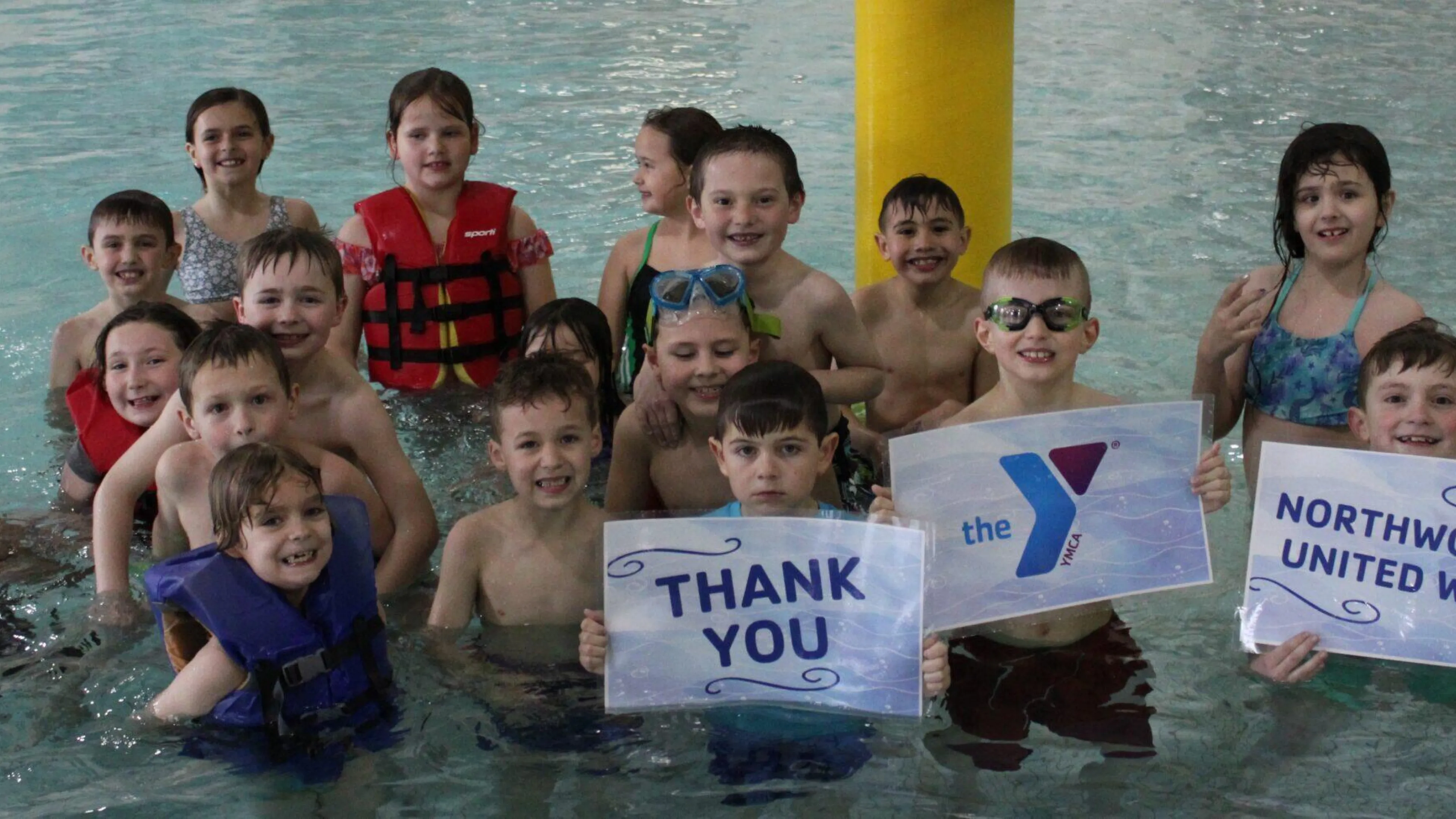 Happy children in a pool, holding signs that say "Thank You," "Northwoods United Way!", and a United Way logo.  Some wear life vests.