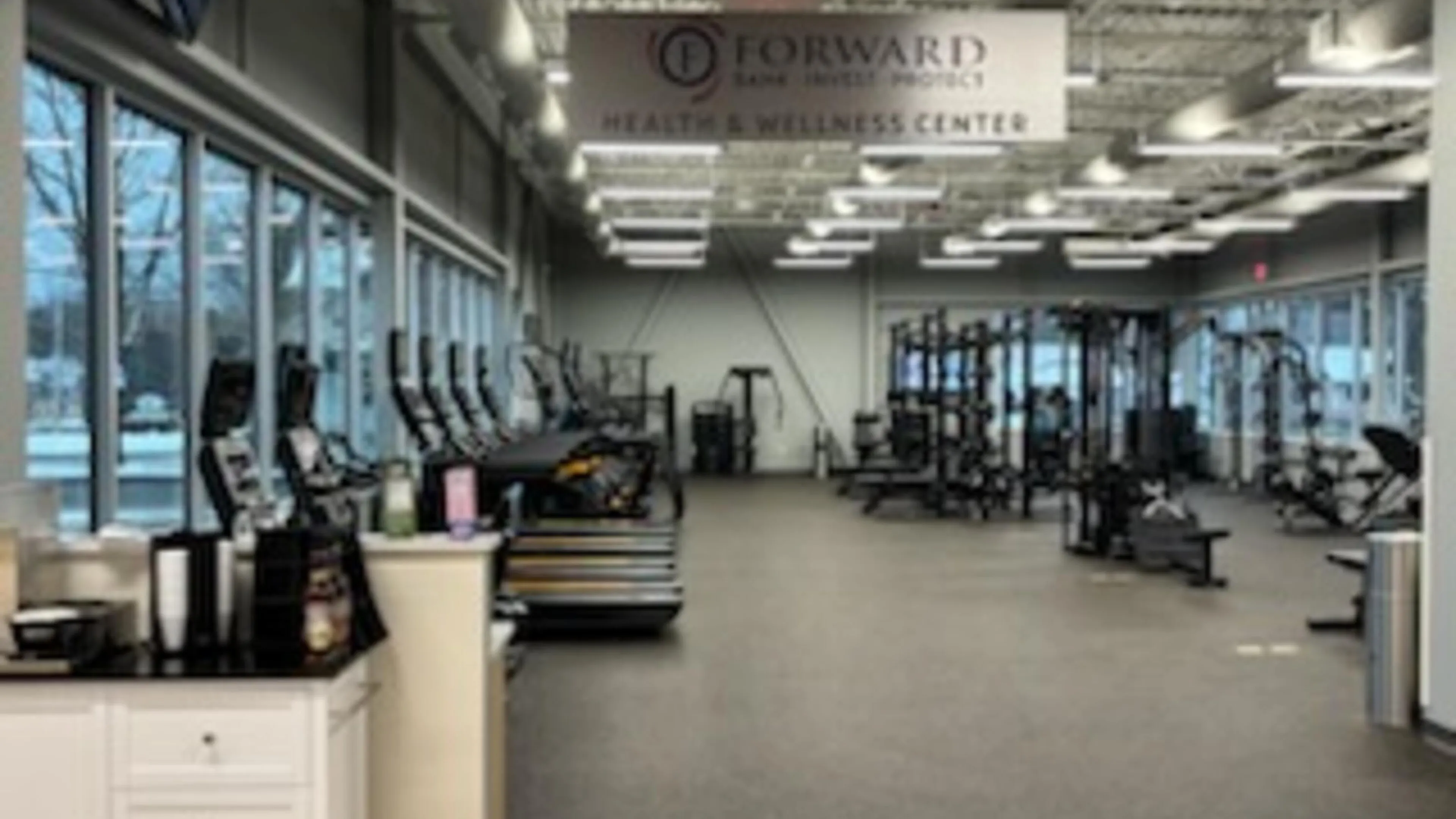 View of a "Health & Wellness Center" through doorway, showcasing cardio machines, weight training equipment, and abundant natural light.