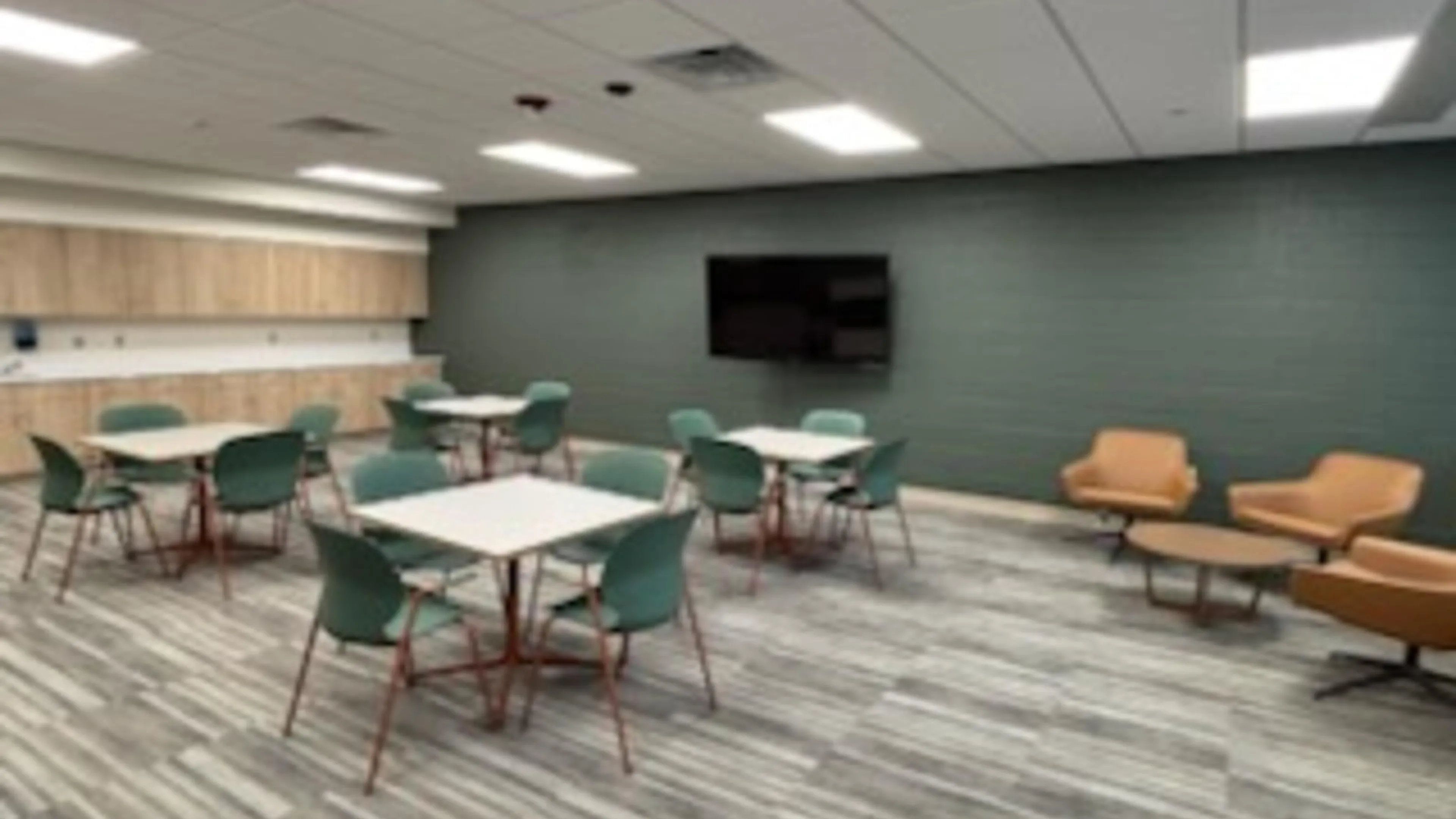 Brightly lit room with tables, chairs, a flat screen TV, and tan leather chairs for after school youth programs.