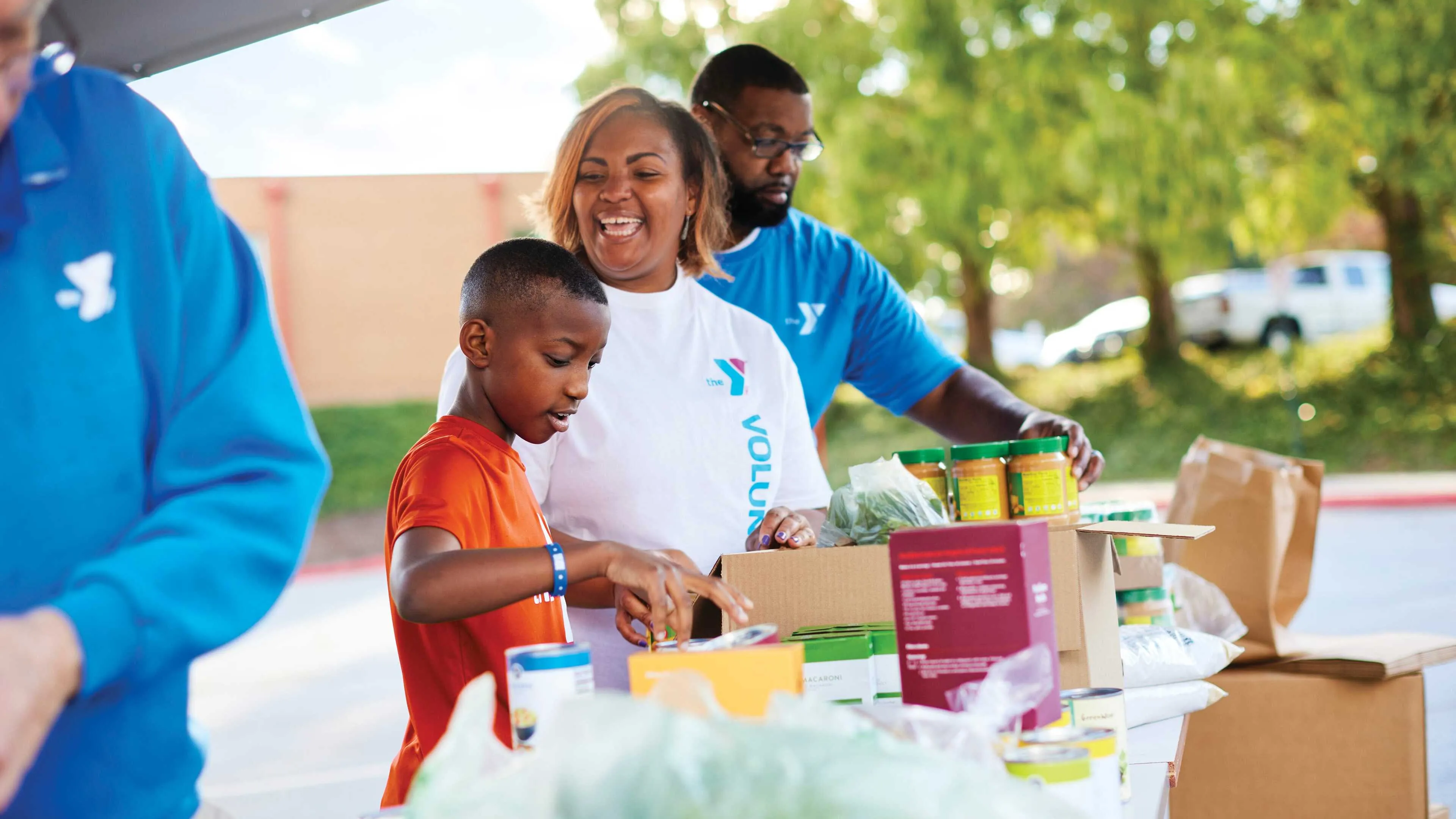 Smiling volunteers, including a boy, sort food donations into boxes.