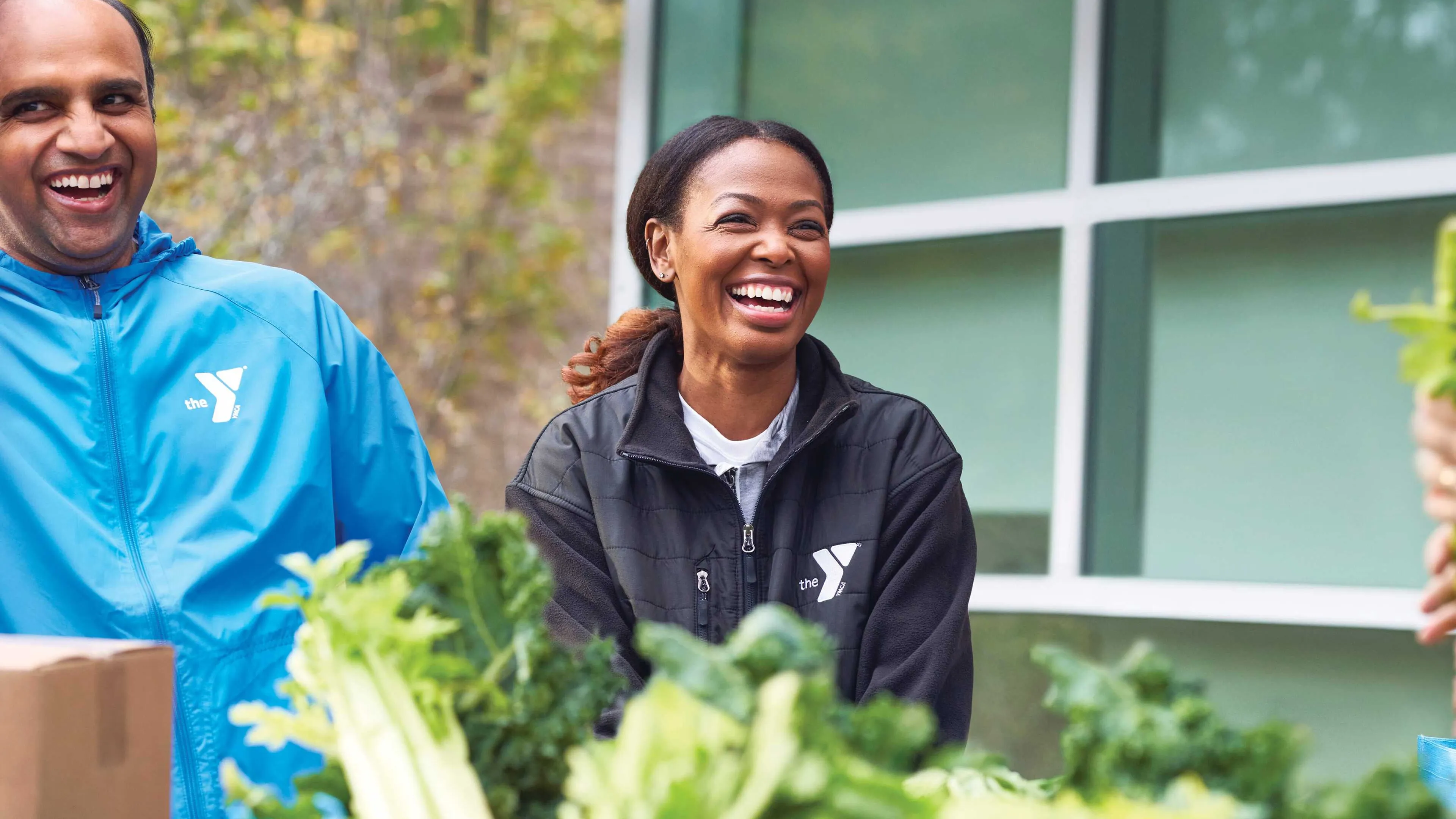 Happy volunteers, wearing organization jackets, unpack fresh vegetables.