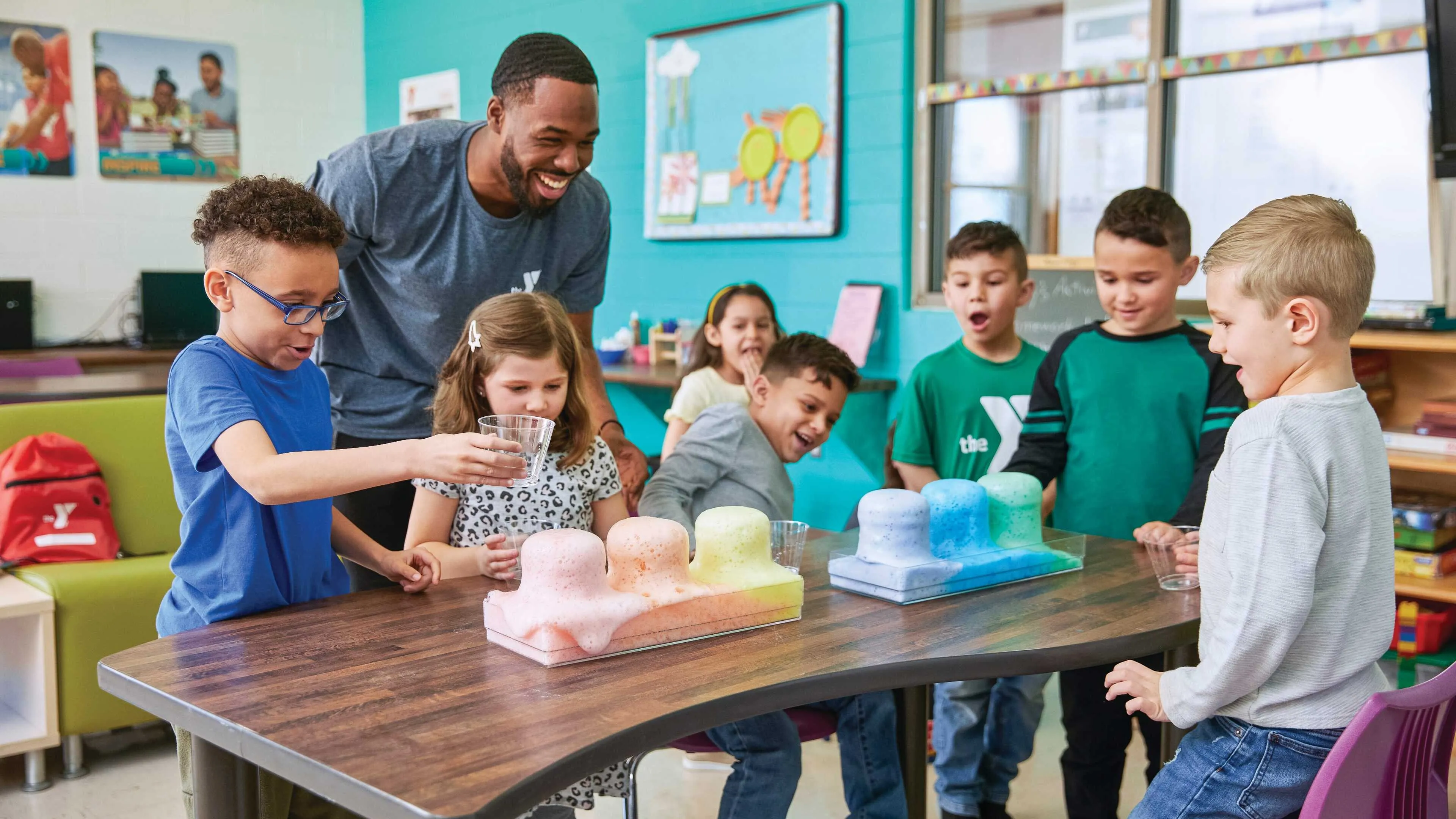 Smiling children conduct a science experiment with pastel-colored substances, guided by a cheerful instructor.
