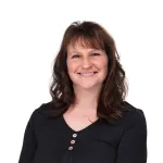 Smiling woman with shoulder-length brown hair, wearing a black long-sleeved shirt.
