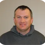 A man with short brown hair smiles while wearing a gray hoodie.
